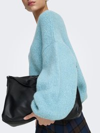 Musta nahkainen käsilaukku, jossa on leijuva muotoilu, pidetty vaaleansinisen paksun neulepuseron vasten. Korostuvat tekstuuri ja rento istuvuus.