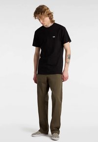 Black cotton t-shirt with a small white logo, paired with olive green pants and black-and-white checkered slip-on shoes.