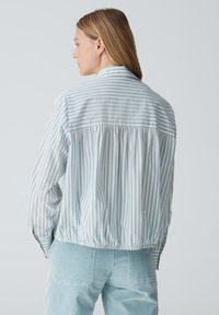 Giacca striata verticale azzurro chiaro e bianca con retro arricciato e polsini abbottonati, realizzata in tessuto morbido e leggero.