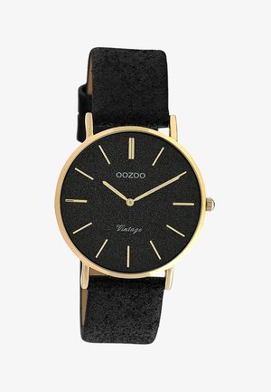 Montre-bracelet OOZOO noire avec boîtier doré, index dorés minimalistes et bracelet en cuir noir texturé affichant l'heure 10:10:09.