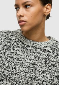 Strikket sweater i sort og hvid med et tekstureret mønster. Ribstrikket rund halsudskæring og løs pasform, der fremhæver detaljerede garn og syninger.