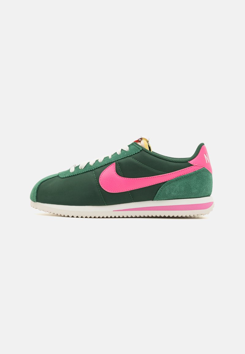 Zelené tenisky so výrazným ružovým logom Nike, bielymi šnúrkami, žltými akcentmi na jazyku a textúrovanou gumovou podrážkou.