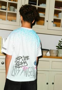 Weißes T-Shirt mit blauem Sprühmuster, schwarzem Schriftzug "DROP SOME BEATS" und "LOS ANGELES" auf der Rückseite; lockere Passform, Baumwollmaterial.