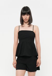 Črn peplum top z tankimi naramnicami, gladkim materialom, kvadratnim izrezom in razširjenim pasom, v kombinaciji s kratkimi črnimi hlačami. Preprost, minimalističen dizajn.