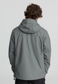 Giacca impermeabile grigia con cappuccio, caratterizzata da una texture liscia e cordini elastici all'orlo. Progettata per l'uso all'aperto.