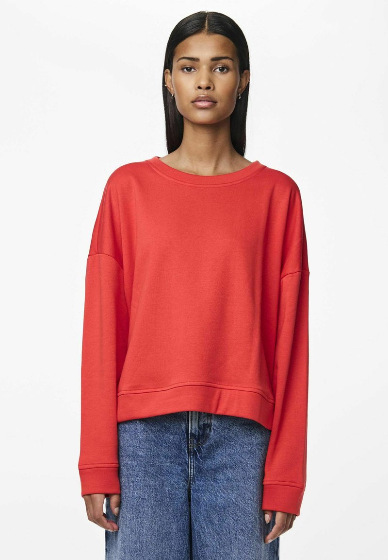 Sudadera roja con un corte relajado, escote ancho y mangas largas. Fabricada con un tejido suave y texturizado, presenta un diseño corto.