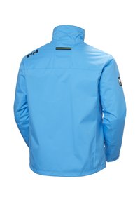 Blauwe waterdichte jas met hoge kraag, een gladde textuur en een zwart logo op de linkermouw. Beschikt over een kleine ventilatieopening aan de achterkant.