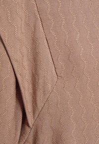 Tessuto rosa chiaro con un motivo a onde testurizzato, che mostra una superficie liscia e una sottile lucentezza. Presenta un dettaglio di cucitura nel design.