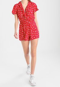Mono corto rojo con un patrón floral, mangas cortas y un diseño envolvente. La cinturilla elástica y los acentos con volantes realzan el detalle.