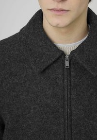 Veste zippée en laine grise avec col et finition texturée. Dotée d'une fermeture éclair en métal et d'un tissu tricot é en dessous.