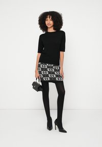 Μαύρο τοπ με κοντά μανίκια, μίνι φούστα σε μαύρο και άσπρο σχέδιο, μαύρα καλσόν και μυτερά μαύρα τακούνια. Μικρή μαύρη τσάντα με λουράκι.