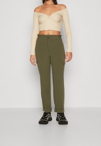 Beige žebrovaný crop top s volnými rameny a dlouhými rukávy, spárovaný s olivově zelenými cargo kalhotami s bočními kapsami a zapínáním na knoflík.