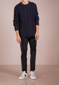 Navyblauer Kabelstrickpullover, schwarze Hose und weiße Sneakers mit farbigen Streifen. Der Pullover hat gerippte Bündchen und einen gerippten Saum für einen strukturierten Look.