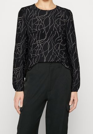 Schwarze Bluse mit langen Ärmeln, die ein wirbelndes Muster aus weißem Faden aufweist. Leichter Stoff, runder Halsausschnitt, lockere Passform, kombiniert mit schwarzen Hosen.