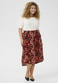 Haut côtelé beige clair à encolure ronde, associé à une jupe fluide longueur genoux avec un motif animal en rouge, noir et rose.