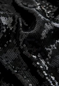 Tissu noir recouvert de petites sequins noirs brillants densément agencés, reflétant la lumière et créant une surface texturée et chatoyante.