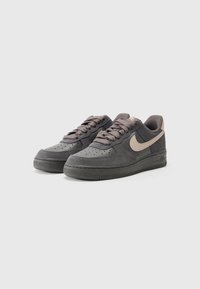 Gray suede sneakers with a textured surface, rounded toe, lace-up design, and a tan swoosh logo on the side. Rubber sole with grip.