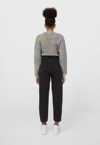 Maglione a maglia multicolore con maniche lunghe, abbinato a jeans neri a vita alta e sneaker bianche, visto da dietro.