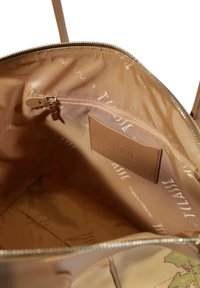 Interno di una borsa in pelle beige che presenta una texture liscia, una tasca con zip e un logo impresso sulla morbida fodera di tessuto con un design mappale.