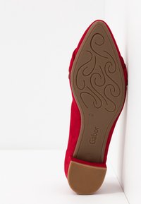 Chaussure plate rouge à bout pointu montrant la semelle avec un motif tourbillonnant décoratif, taille 4,5 et marque Gabor sur fond blanc.