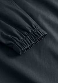 Tume kangas lähivõte, kus on näha kokkusurutud elastne mansett koos detailse õmblusega varrukal või pükste säärel.