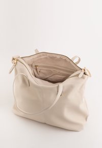 Beige læderhåndtaske med en tekstureret overflade, en lynlåslukning på toppen, og et rummeligt interiør med en lynlåslomme og glat foring.