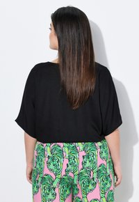 Top corto nero realizzato in tessuto leggero, abbinato a pantaloni rosa con un vivace motivo a tigre verde. Texture liscia e vestibilità comoda.