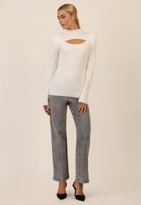 Hvid ribbet langærmet top med en udskåret neckline, parret med lysegrå vidde bukser med et prikket mønster og sorte hæle.