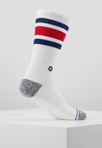 Vita ankelsocka med röda och marinblå ränder högst upp, grå texturerad häl och en liten logotyp på sidan.
