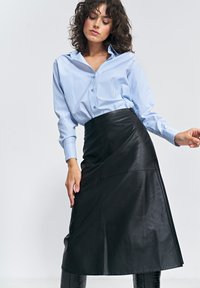 Czarna skórzana spódnica o kopertowym kroju, zestawiona z koszulą na guziki w jasnoniebiesko-białe paski. Gładka faktura, długość do kolan, eleganckie dopasowanie.