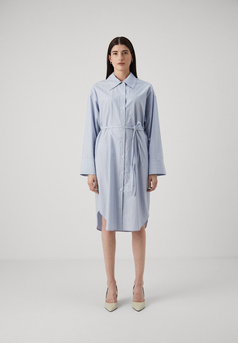Abito camicia a righe blu chiaro, con colletto, chiusura a bottoni sul davanti, cintura in vita e maniche lunghe con ampi polsini. Tessuto liscio con spacchi laterali.