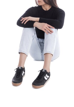 Zapatillas deportivas negras con acentos blancos, que cuentan con un upper texturizado, cierre de cordones y suelas de goma, combinadas con jeans de color azul claro.