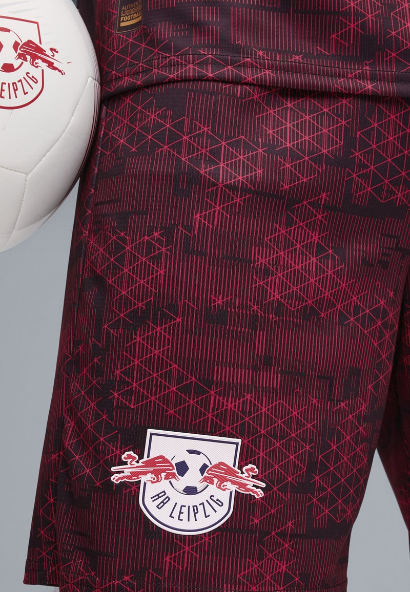 Bermudas rojas y negras con un diseño geométrico, adornadas con el logo del RB Leipzig y un balón de fútbol blanco, elaboradas en material ligero.