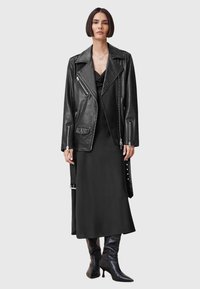Zwarte leren motorjack met ritszakken, gedragen over een strakke zwarte jurk. Hoge zwarte hakken boots maken de outfit compleet. Eenvoudige zilveren ketting.