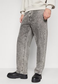 Jeans de mezclilla gris con un corte relajado, que presentan una textura desgastada y un diseño de pierna recta. Combinados con botas de plataforma negras.