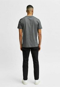 Grå kortärmad T-shirt med en avslappnad passform, kombinerad med svarta byxor och vita sneakers. T-shirten har en slät textur och klassisk form.