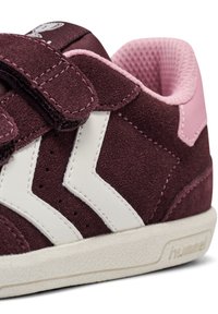 Mörkröda mockaskor med vita läderdetaljer, kardborreband och strukturerad gummisula. Har ventilationshål och logotypdetalj.