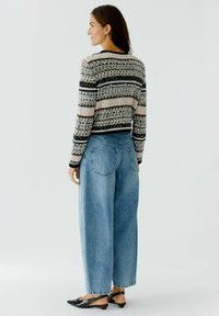 Gebreide trui met een geometrisch patroon in zwart, roze en zilver, gecombineerd met lichtblauwe high-waisted wijde jeans en zwarte slingback schoenen.