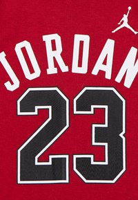 Rødt stof med hvid "JORDAN" tekst og sort "23" omringet af hvid, med et Jumpman-logo. Glat, atletisk skjorte tekstur.