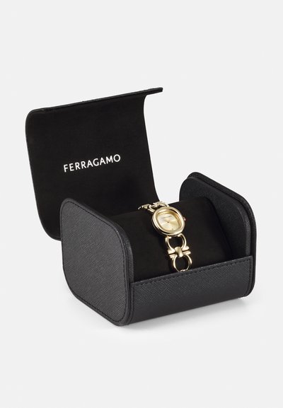 Gold watch with round face and chain link strap, displayed in sleek black box featuring soft interior and Ferragamo logo on lid.