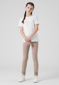 Witte katoenen T-shirt gecombineerd met lichtbeige leggings. De leggings hebben gerimpelde details bij de enkels. Model draagt witte sneakers.