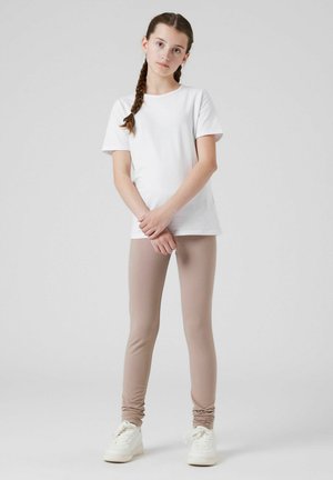 T-shirt en coton blanc associé à un legging beige clair. Les leggings sont dotés de détails froncés au niveau des chevilles. Modèle portant des baskets blanches.