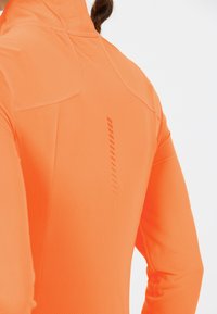 Orange præstationstop med høj krave og åndbart tekstureret stof. Har en slim fit og lodret reflekterende detalje på ryggen.