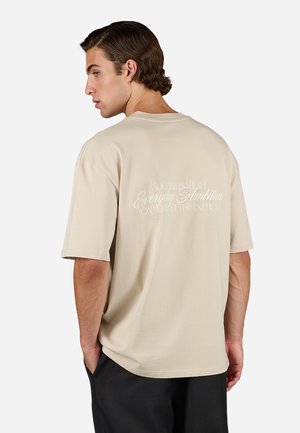 Camiseta de algodón beige con mangas cortas y un corte relajado, con texto blanco en la parte posterior que muestra una cita motivacional.