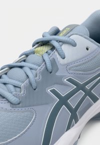 Lichtblauwe hardloopschoen met een gestructureerde bovenkant, contrasterende grijze accenten en een witte tussenzool. Bevat veters en gestreepte, ademende secties.
