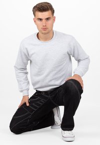 Felpa grigia in cotone con maniche lunghe e colletto a girocollo, abbinata a jeans neri con cuciture diagonali e dettagli bianchi.