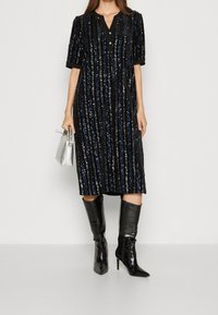 Svart paljetklänning med vertikala ränder, korta ärmar, V-ringning och knappar. Kombinerad med knähöga svarta klackstövlar och en silverväska.
