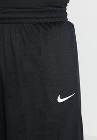 Svarta mesh atletiska shorts med en texturerad yta, med en vit Nike-logotyp på nedre högra sidan och ett elastiskt midjeband.