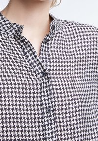 Zwart-witte houndstooth patroon shirt met een knoopsluiting kraag, voorzien van twee zwarte knopen en een gladde textuur.