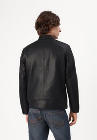 Zwart leren jasje met gewatteerde schouderaccenten en een staande kraag, gecombineerd met blauwe spijkerbroek met contrasterende stiksels op de zakken.